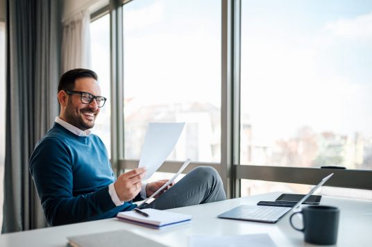 Smiling business professional reading documents while sitting at Man Reviewing Quote